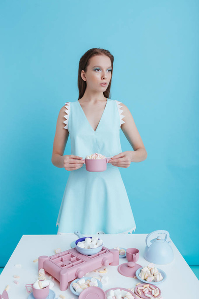 Beautiful young woman standing and holding plastic dishes with marshmallows - Фото, изображение
