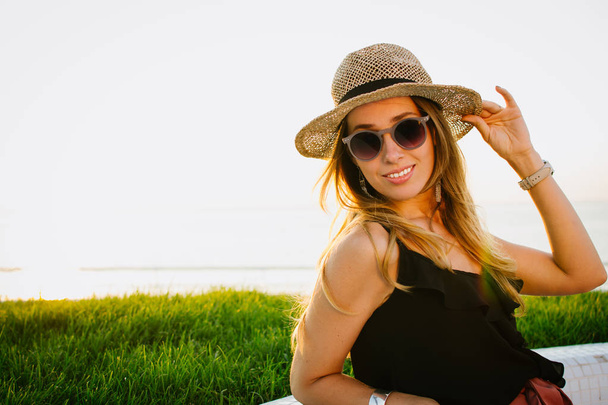 Pretty young woman in hat and glasses smiling and posing at seafront - Foto, imagen