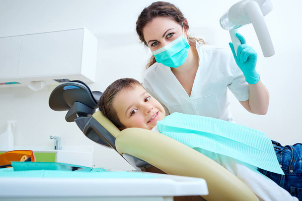 Beautiful kid boy smiling in dentists chair the office treats teeth. Doctor mask and baby looks at camera. - Foto, imagen