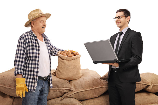 Farmer and a businessman with a laptop in front of a pile of burlap sacks - Photo, image