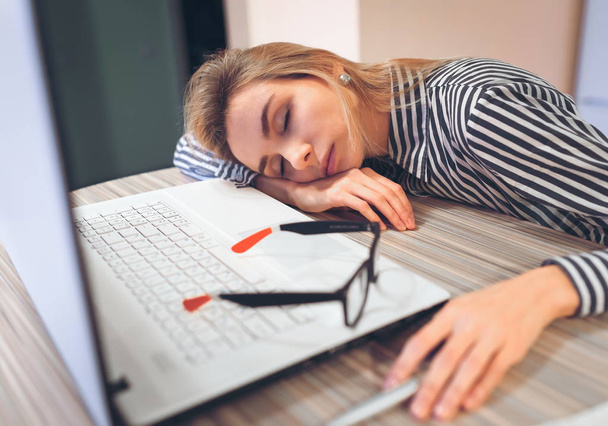 Freelancer meisje slapen op de baan aan de tafel in de buurt van de laptop - Foto, afbeelding