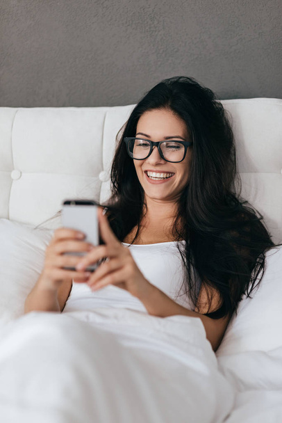 Beautiful woman holding smartphone in bed  - Foto, Imagem