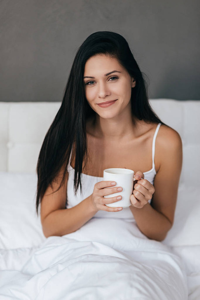 Gorgeous woman holding cup in bed - 写真・画像
