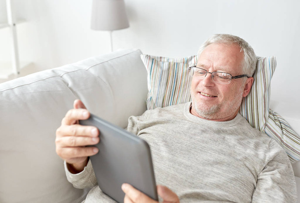 senior man with tablet pc lying on sofa at home - Foto, imagen