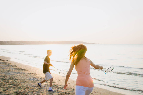 Mom and son playing badminton at the sea coast during sunrise or sunset - Valokuva, kuva