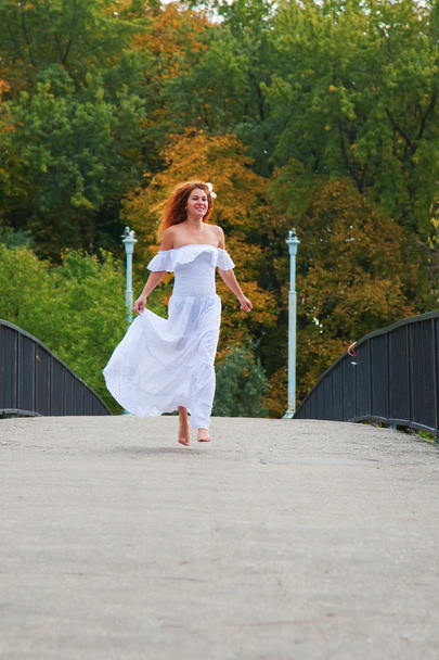 Рудоволоса молода жінка, одягнена в білу сукню або наречена біжить через міст
 - Фото, зображення