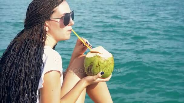 Young woman drinks coconut milk against ocean - Séquence, vidéo