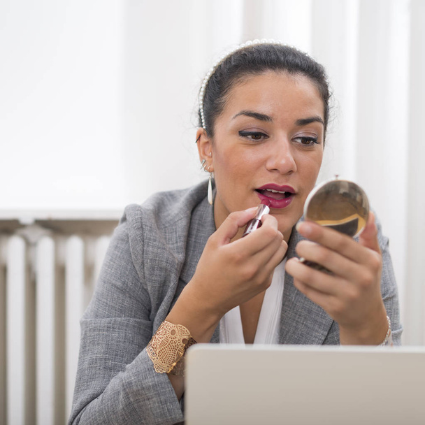 Portrait of businesswoman applying lipstick in office before mee - Photo, Image