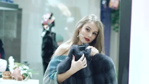 Hermosa chica elige un abrigo de piel en la tienda
 - Metraje, vídeo