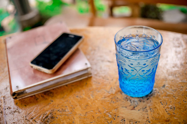 Blue Glass with water Notebook and Smartphones on a wooden table. - Фото, изображение