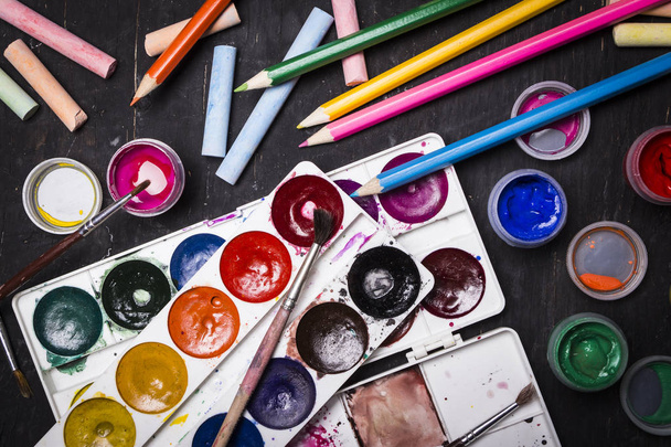 Bright multi-colored paint, pastels, crayons, pencils, brushes on a black wooden background. Set for the artist. Education. - Photo, Image