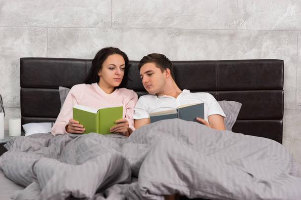 Young couple reading each other books while lying in the bed and - Foto, Imagem