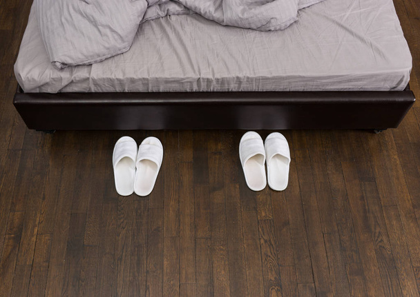Domestic white slippers are beside the bed  - 写真・画像