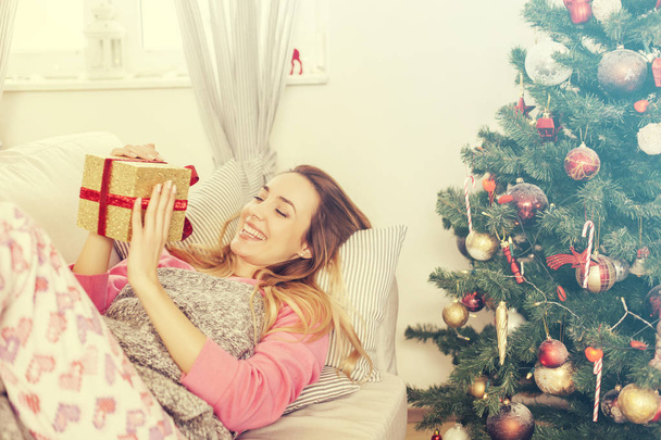 woman lying on the sofa holding a Christmas present - Foto, afbeelding
