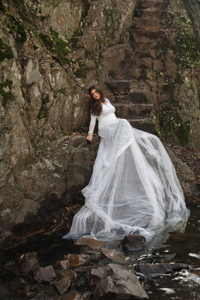 Jonge vrouw met blauwe ogen gekleed bruid zittend op een stenen trap op het platteland. - Foto, afbeelding