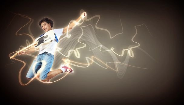 Young man playing on electro guitar and jumping - 写真・画像