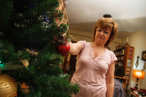 Ενήλικη γυναίκα, μητέρα, διακόσμηση χριστουγεννιάτικο δέντρο με πολύχρωμες μπάλες. - Φωτογραφία, εικόνα