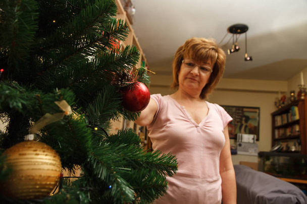 Ενήλικη γυναίκα, μητέρα, διακόσμηση χριστουγεννιάτικο δέντρο με πολύχρωμες μπάλες. - Φωτογραφία, εικόνα