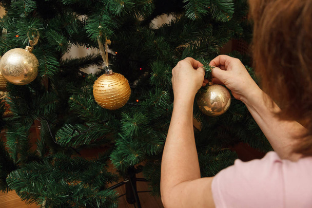 Adult woman, mother, decorating Christmas tree with colorful balls. - Φωτογραφία, εικόνα