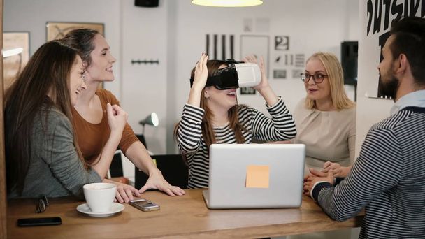 first experience with virtual reality glasses young team supports young beautiful brunette girl in modern startup office - Foto, imagen