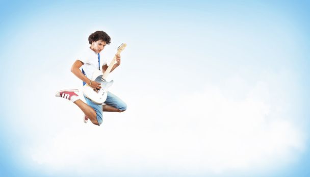 Young man playing on electro guitar and jumping - 写真・画像
