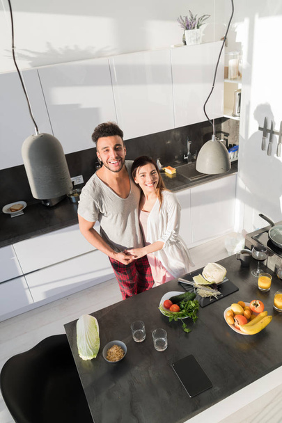 Young Couple Embrace In Kitchen, Hispanic Man And Asian Woman Hug Top Angle View - Foto, imagen