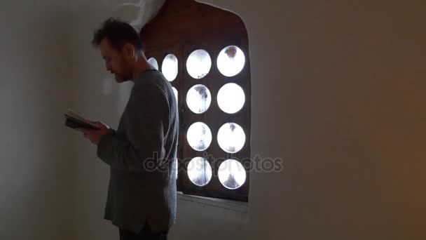 Hombre de pie en el libro de la ventana en sus manos Turista en la capilla de la iglesia Dentro de la cueva de tiza velas están ardiendo Tour a Svyatogorsk Turismo en Ucrania
 - Metraje, vídeo