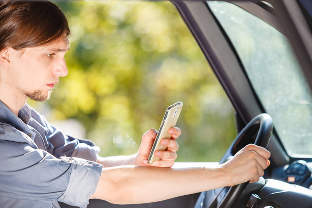 Mężczyzna korzystający z telefonu podczas jazdy samochodem. - Zdjęcie, obraz