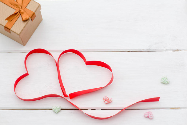 red ribbon lying in the shape of two hearts and gift box - Foto, imagen