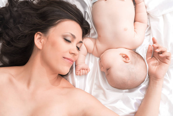 Young mom with newborn baby sleeping in bed - Valokuva, kuva