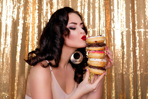 молодая, красивая, привлекательная, темноволосая женщина с красочными, вкусными, застекленными пончиками на золотом фоне
 - Фото, изображение