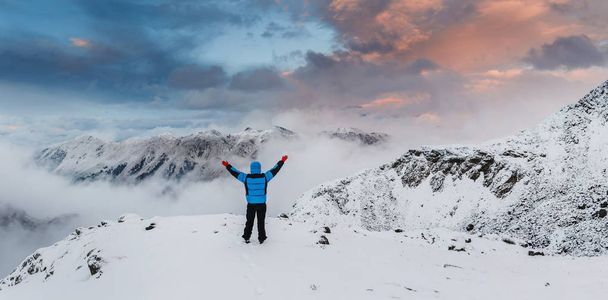 Caminhante com as mãos levantadas fica no vale da montanha e desfrutar de paisagem de inverno ao nascer do sol
 - Foto, Imagem