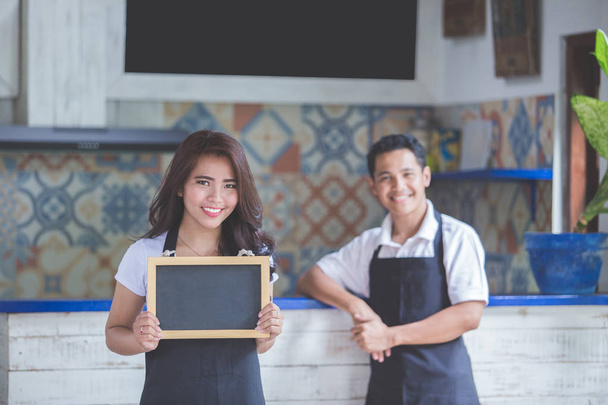 female cafe worker smiling and holding blank blackboard - Foto, afbeelding