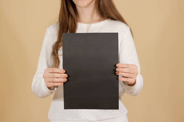 Girl holding black A4 blank paper vertically. Leaflet presentati - Photo, Image
