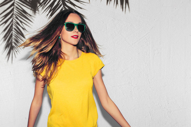 Summer Portrait of Hipster Fashion Smiling Girl with Hands on Hips at palm tree Background. Fun positive young smart woman in glasses and colorful yellow shirt smiling with perfect teeth. - Foto, imagen