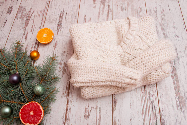 Pullover aus Milchwolle auf einem hölzernen Hintergrund. Zitrusfrüchte, Tannenzweig mit Weihnachtsdekoration. Modisches Konzept, Draufsicht - Foto, Bild