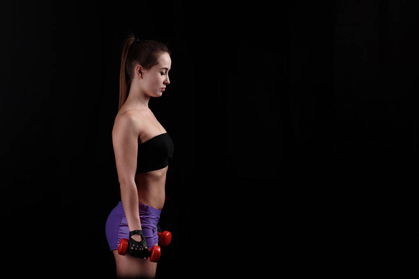 Sport girl holding a dumbbell on black background. - Valokuva, kuva