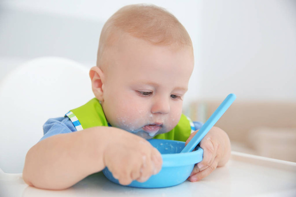 Little baby eating from bowl with spoon indoors - Valokuva, kuva