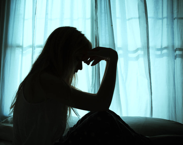 Silhouette einer Frau, die am Fenster im Bett sitzt - Foto, Bild