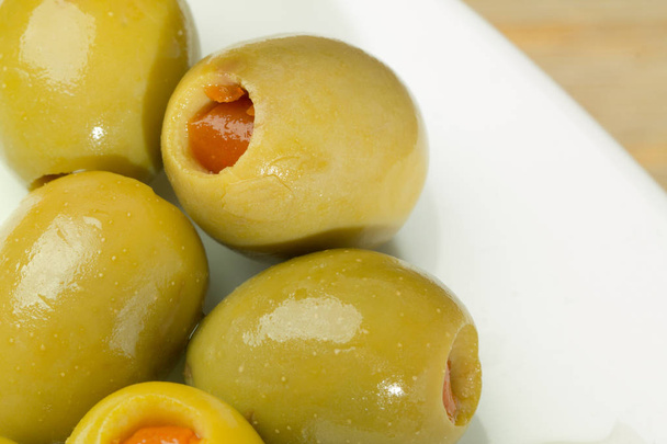 White plate of green olives filled with red paprika standing at wooden table background. - Photo, Image