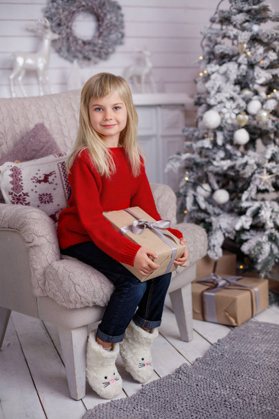 Cute little child girl with present. Kid holds a magic gift box near Christmas tree indoors. - Foto, imagen