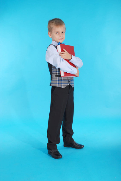Niño en uniforme escolar sosteniendo un libro rojo
 - Foto, Imagen