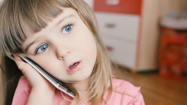 Malé dítě dítě stejně jako dospělý, mluví na smartphone, zatímco sedí na koberci v jejím pokoji - Záběry, video