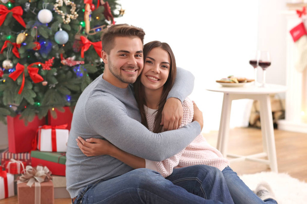 Young couple near Christmas tree indoors - Foto, imagen