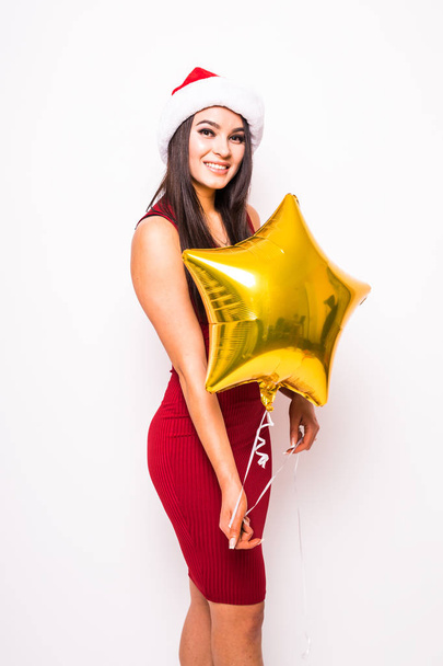 Pretty young woman in red dress and santa christmas hat with gold star shaped balloon  - 写真・画像