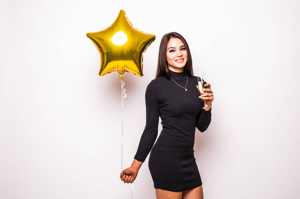 Mooie jonge vrouw in zwarte jurk met gouden ster vormige ballon glimlachend en drinken champagne - Foto, afbeelding