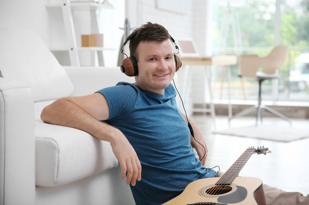 Young man sitting with a guitar on the floor and listening to music on headphones - Φωτογραφία, εικόνα