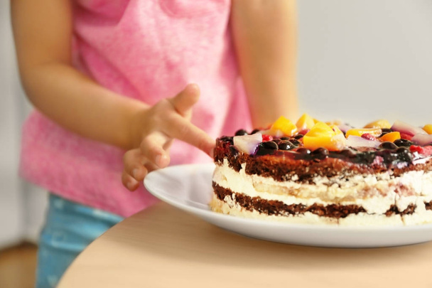 Little girl tasting sweet cake left on kitchen table, close up view - Fotografie, Obrázek