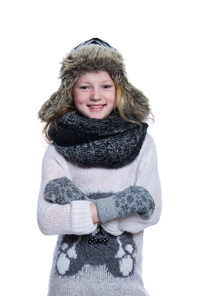 Happy cute kid posing in the studio. Wearing winter clothes. Knitted woolen sweater and mittens. Ear flaps fur cap. Isolated on white background. - Fotografie, Obrázek