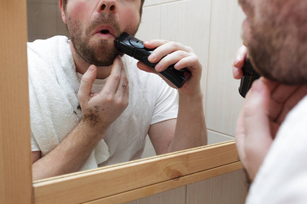 Jeune homme avec une barbe rasez chaume avec rasoir électrique. - Photo, image